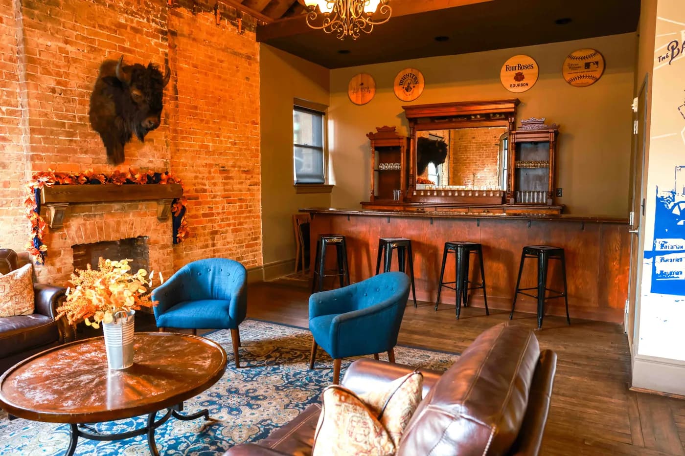 Blue armchairs and a leather sofa by the fireplace, with the bar and bourbon barrel heads behind
